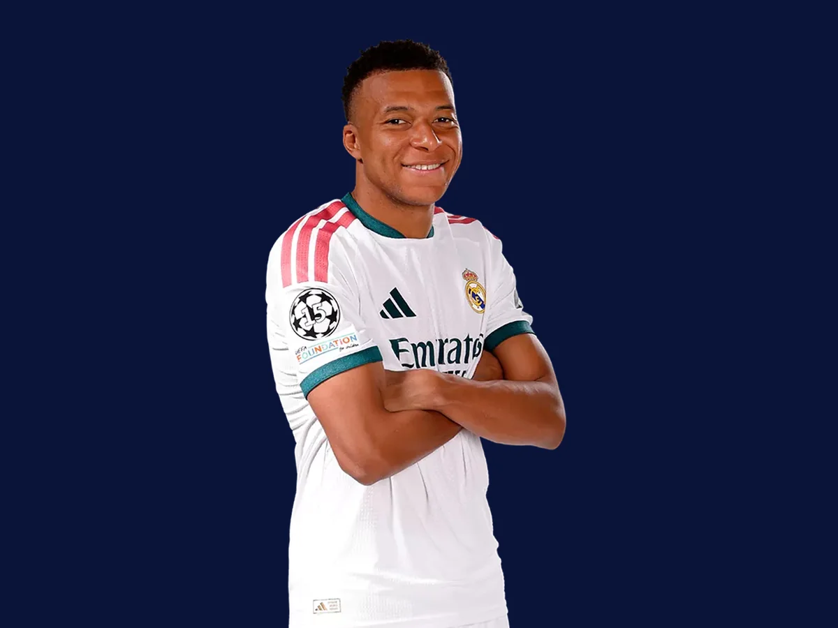 Kylian Mbapp&eacute; souriant, bras crois&eacute;s, en maillot blanc du Real Madrid.